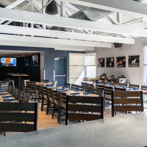 Large private event room with long communal tables set with blue napkins, high ceilings, and TVs.