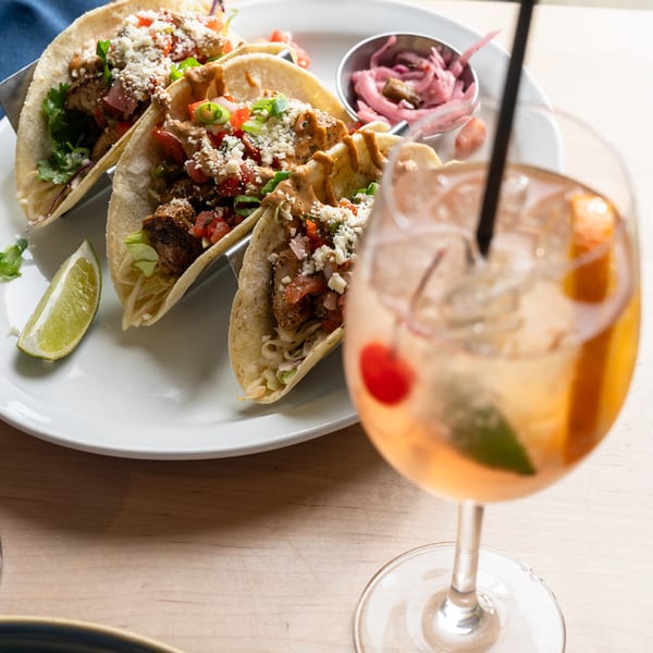 Blackened chicken tacos with pico and pickled onions beside a cocktail.