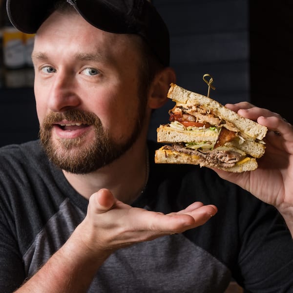 Smiling guest presenting a club sandwich.