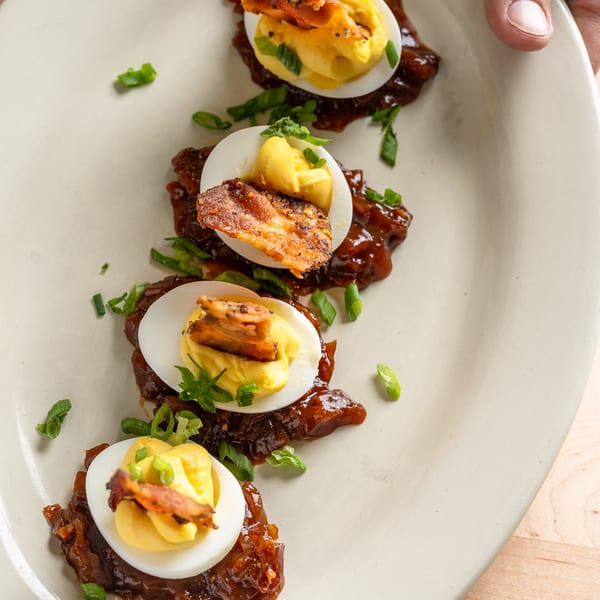 Deviled eggs topped with crispy bacon and scallions over bacon jam.
