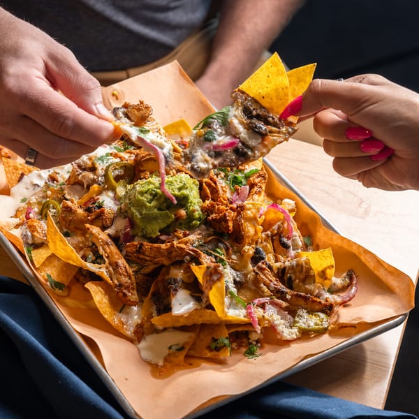 Two guests sharing a tray of loaded chicken nachos.