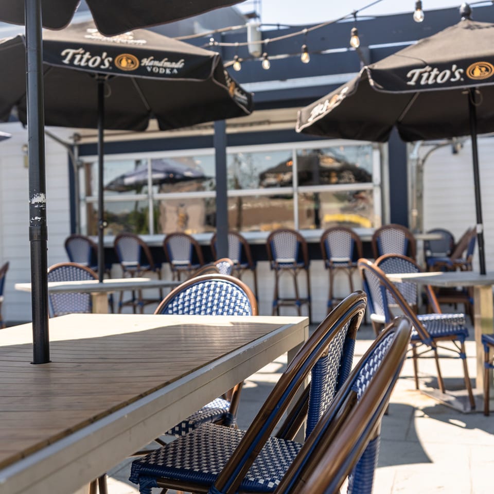 Sunny outdoor patio with umbrellas and blue bistro chairs.