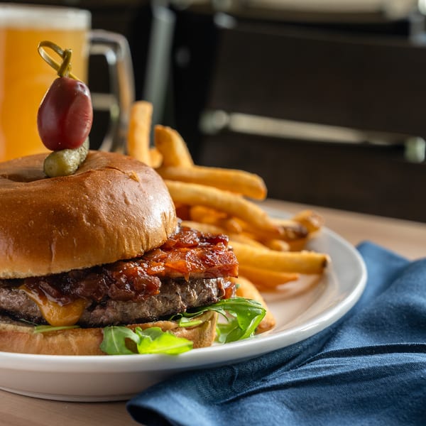 A bacon jam cheeseburger with fries and a beer on a wooden table.