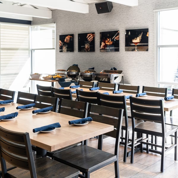 Private dining room with wooden tables set with blue napkins and a buffet station by the windows.