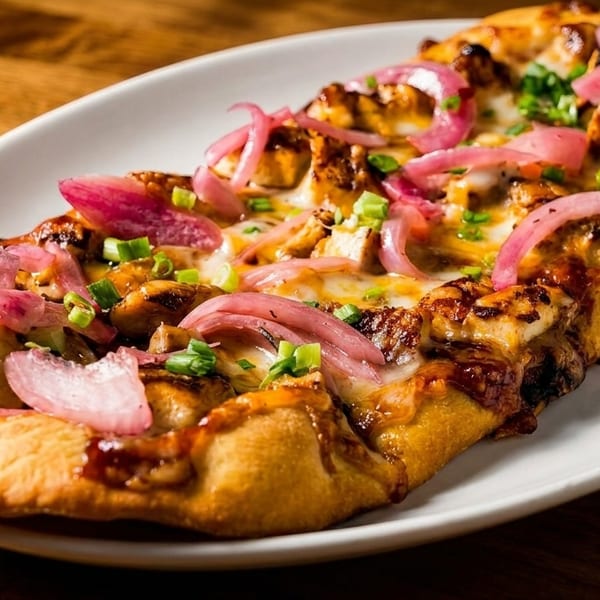 BBQ chicken flatbread with melted cheese, red onions, and green onions on a white plate.