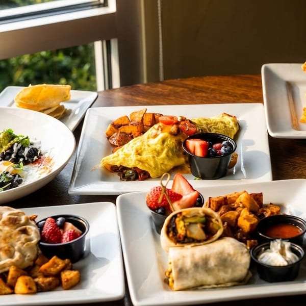 A table laden with various breakfast dishes, including omelets, waffles, pancakes, and breakfast burritos.