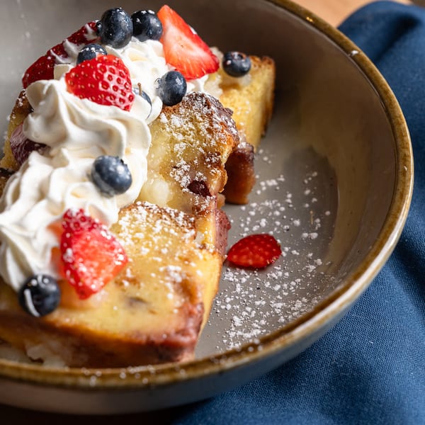 Berry-topped French toast with whipped cream and powdered sugar.