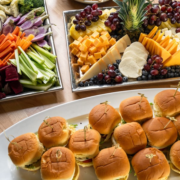 Party spread with mini sliders, a vegetable crudite tray, and a cheese and fruit board.